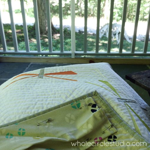 Day 112: 365 Days of Handwork Challenge — Stitching a sleeve on this Dragonfly Dance Quilt so it can go off to Urban Sew Fabric Shop for their booth at in Grand Rapids American Quilt Week. The weather is beautiful on my front porch today and our plynosaur (plywood dinosaur) is keeping me company. Whole Circle Studio — 365 Days of Handwork Challenges