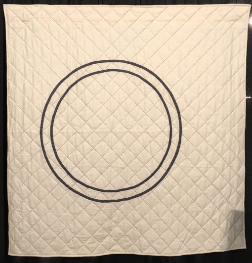 "Counterpart" by Riane Menardi Morrison Statement: "This quilt is my modern take on a Wedding Ring quilt. After getting married in fall 2017, I started designing and making quilts that represent my idea of home and family. This quilt design was inspired by two wedding rings—mine and my husband's. The 1/2 rings are appliqued on a wholecloth background. The quilt is hand-quilted using large sashiko thread in two colors. The quilting motif emanates from the center of the rings, representing two lives coming together.” [Design Source: Original Design] displayed in the 2018 Modern Quilt Showcase sponsored by the Modern Quilt Guild at the International Quilt Festival in Houston