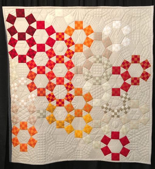 "Unchained Melody" by Jackie Benedetti. Quilted by Dionne Matthies-Buban. Statement: "I've always been intriqued by the 1930s pattern Jack's Chain and love how different the pattern looks depending on color placement. I was inspired to make a modern rendition using solids, lots of negative space, and my favorite colors. Dionne's quilting helped highlight the background blocks. Minimal quilting of the Nine Patch blocks helped make them pop. The entire top was hand-pieced except for the Nine Patch blocks.” [Design Source: Jack's Chain pattern] displayed in the 2018 Modern Quilt Showcase sponsored by the Modern Quilt Guild at the International Quilt Festival in Houston