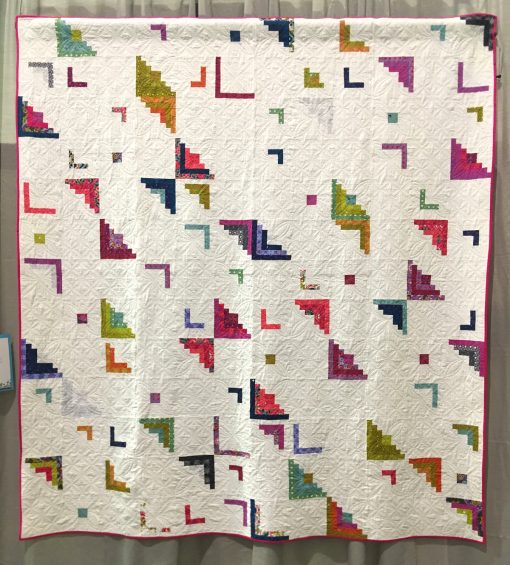 Modern quilt featured at QuiltCon 2019 — “Peeling Away” by Betsy Ryan @rryan3. Quilted by Janice Roy Statement: “This quilt is an adaptation of the traditional Log Cabin quilt block, the quintessential American design. It represent log cabins on the prairie with the center squares for the hearth, light values on one side for the sunny side of the house, and dark values on the opposite side for the shady side of the house. I wanted this quilt to have a lot of negative space, to be less cluttered, to be freeing. I started out with more complete log cabin shapes and then removed more color and left more negative space. 