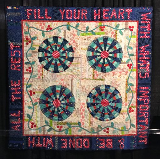 "Wheel of Fortune" by Pat Sloan. Quilted by Cindy and Dennis Dickinson <br>Statement: "I wanted to do a Dresden block made up of trips of different widths. I had accumulated boxes of leftover sample strips for creating my round Dresden. Filling the center with a snazzy red polka dot, my Wheel of Fortune came to life." [Design Source: Aurifil 50wt large cotton thread spools | Techniques: Machine pieced and quilted] 