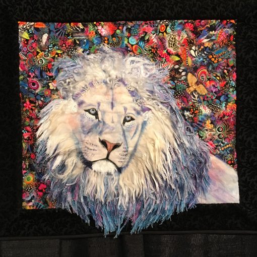 "A Promise Kept" by Lorraine Turner <br>Statement: "I met this white lion in a South African sanctuary in 2015. Although he no longer lives in the physical plane, this majestic soul visits me in meditation. His appearances tend to coincide with my wondering if my art is raining awareness of the endangered animals. Aurifil thread as well as alpaca, llama, and lamb's locks are blended into his magnificent mane and his whiskers are horsehair." [Design Source: Meditation visitations | Techniques: Hand embellished, felted, raw-edge appliqued, embroidered] 