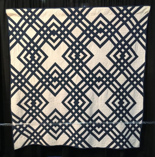 Carpenter's Square by Unknown Maker. An indigo and white Carpenter's Square is distinguished by an unusual diagonal block. Constructed by hand and machine, the quilt features double line hand quilting in a windowpane pattern with a hand stitched binding. On loan from the collection of International Quilt Festival. | Techniques: Hand pieced and quilted, machine pieced | Design Source: Interlocked Squares | Photo taken at 2019 International Quilt Festival