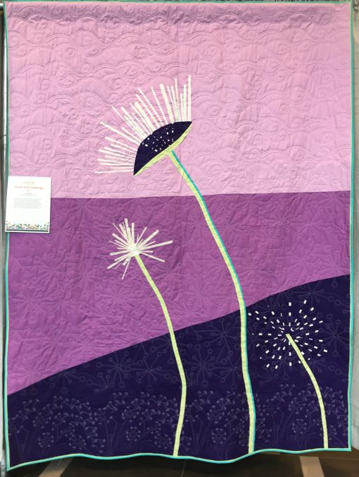 On the Breeze by the Prince Edward Island Modern Quilt Guild (Stratford, Prince Edward Island, Canada) Statement: As a small guild, we collaborated on the concept, as it embodies the principles of a modern quilt and offered a challenge for our members. While working on the design, the dandelions were abundant on the Island. Over a few sew-ins and after careful consideration along the way, members working on this quilt were enjoying improve piecing and trying different techniques to represent the flower getting ready to be on the breeze in search of new grounds. This quilt was truly a collaborative effort. Pieced by Heather, Cathy, Dawn, Jean, Janet, Velda, and Linda. Designed by Heather Jarman and machine quilted by Colleen Henderson. Displayed at QuiltCon 2019 in Nashville, Tennessee.