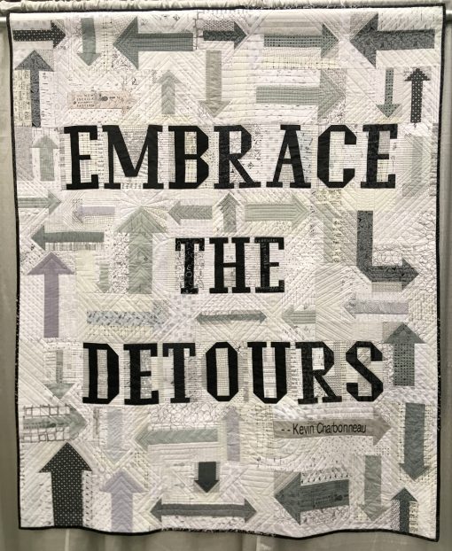 “Embrace the Detours” by Washington DC Modern Quilt Guild @dcmqg Statement: “Embrace the Detours was conjured by a small group within DCMQG who jumped from the challenge description to brainstorming about words for the quilt. We settled on Kevin Charbonneau’s iconic admonition to Embrace the Detours! Over 30 DCMQG members created the arrows and letters of the quilt. The next step was the incredible ruler quilting by Sarah Thomas @sariditty . Thanks to all DCMQG members for this impressive group effort.” Modern quilt featured in the Charity Quilts category at QuiltCon 2020 in Austin, Texas presented by the Modern Quilt Guild.