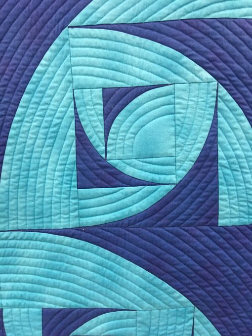 detail of “Breakers” by Pat Forster Statement: “The block is my original design—a fractal based on the Drunkard’s Path block. Contrasting blues, the block that evokes water in turmoil, the block arrangement that shows breakers rolling to shore, the quilt title, and the manta ray backing fabric, all complement each other. Machine pieced and quilted.” Modern quilt featured in the Piecing category at QuiltCon 2020 in Austin, Texas presented by the Modern Quilt Guild.