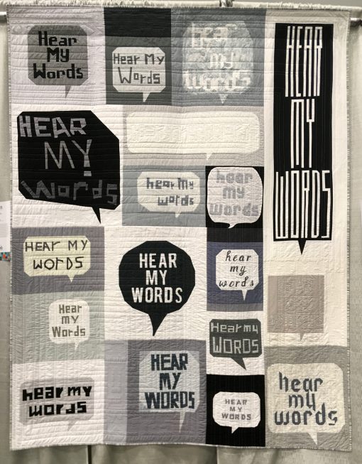 “Hear my Words” by Vancouver Modern Quilt Guild @vancouvermqg Statement: “Every human being deserves to feel respected and valued in life, and to have their needs and view points heard. If we spend more time listening to each other, we will understand each other better, and in the end all feel more connected. We don’t always have to agree, but we do need to have empathy, and embrace the fact that diversity and differences are what makes our world both beautiful and interesting. This is the only way to find peace in our hearts. This quilt symbolizes those voices that have been crushed by prejudice, fear or pain experienced in life. Each maker asked to piece a block with “HEAR MY WORDS” in a speech bubble, with the style they chose visually representing how they personally felt about having their words heard. Some blocks are big, bold and loud, others are small, quiet and introvert. These are based on each maker’s life experiences. The goal was to make the viewer contemplate what words it is that they themselves are feeling need to be heard, and also to remind them to take the time to listen the next time someone shares their thoughts. Pieced by the members of the VMQG. Longarm quilted by Laura Gates @poppyseedquilting “ Modern quilt featured in the Charity Quilts category at QuiltCon 2020 in Austin, Texas presented by the Modern Quilt Guild.