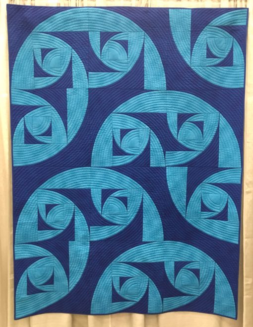 “Breakers” by Pat Forster Statement: “The block is my original design—a fractal based on the Drunkard’s Path block. Contrasting blues, the block that evokes water in turmoil, the block arrangement that shows breakers rolling to shore, the quilt title, and the manta ray backing fabric, all complement each other. Machine pieced and quilted.” Modern quilt featured in the Piecing category at QuiltCon 2020 in Austin, Texas presented by the Modern Quilt Guild.