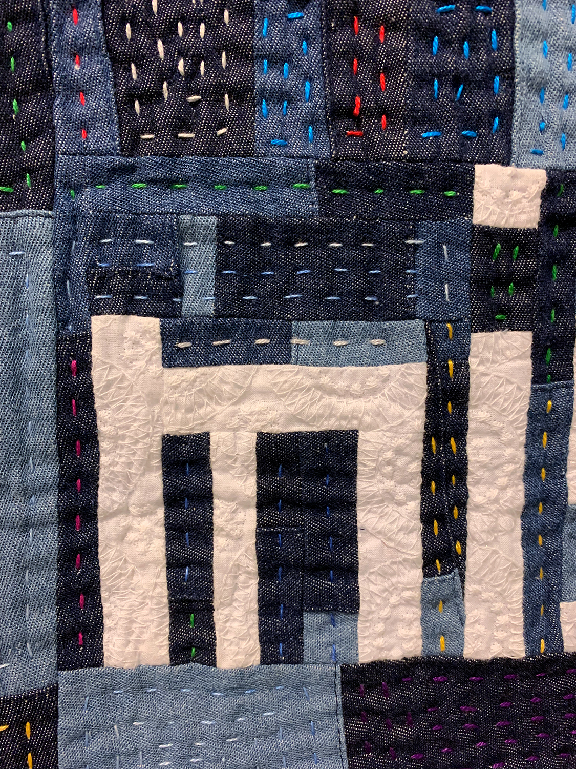 detail of improvisational quilt made with denim and cotton stating "i miss hope" in the middle