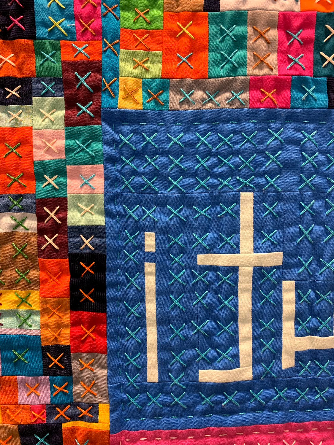 detail of colorful modern quilt with the words "uoy evol i tub" in the lower right corner