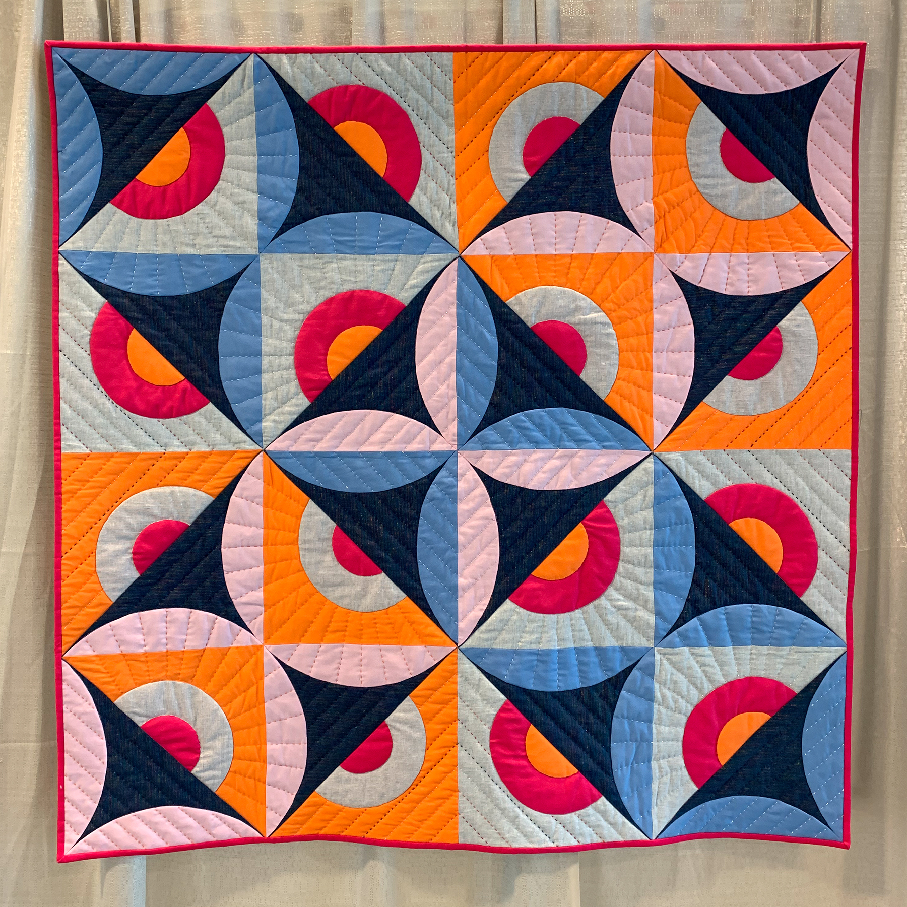 "Cosmic Orange Peel" by Laura Ward Statement: “This quilt is sparkles and sunshine and symmetry. All the curved shapes you see are appliqued, an dI couldn't resist the combination of metallic linen and metallic thread to accent them. I tried out a new idea when making the half circle shapes on this quilt. I started with squares of fabric and hand appliqued 2 layered circles on top. I put another square on top of this, sewed 2 diagonal lines, and essentially made 2 big half square triangle units. (P.S. It feels very wrong to cut your carefully hand appliqued blocks in half, but it all worke dout in the end). More orange-peel-esque curves were layered on to make the pink and blue applique circles crossing through the middle. featured in the Applique category
