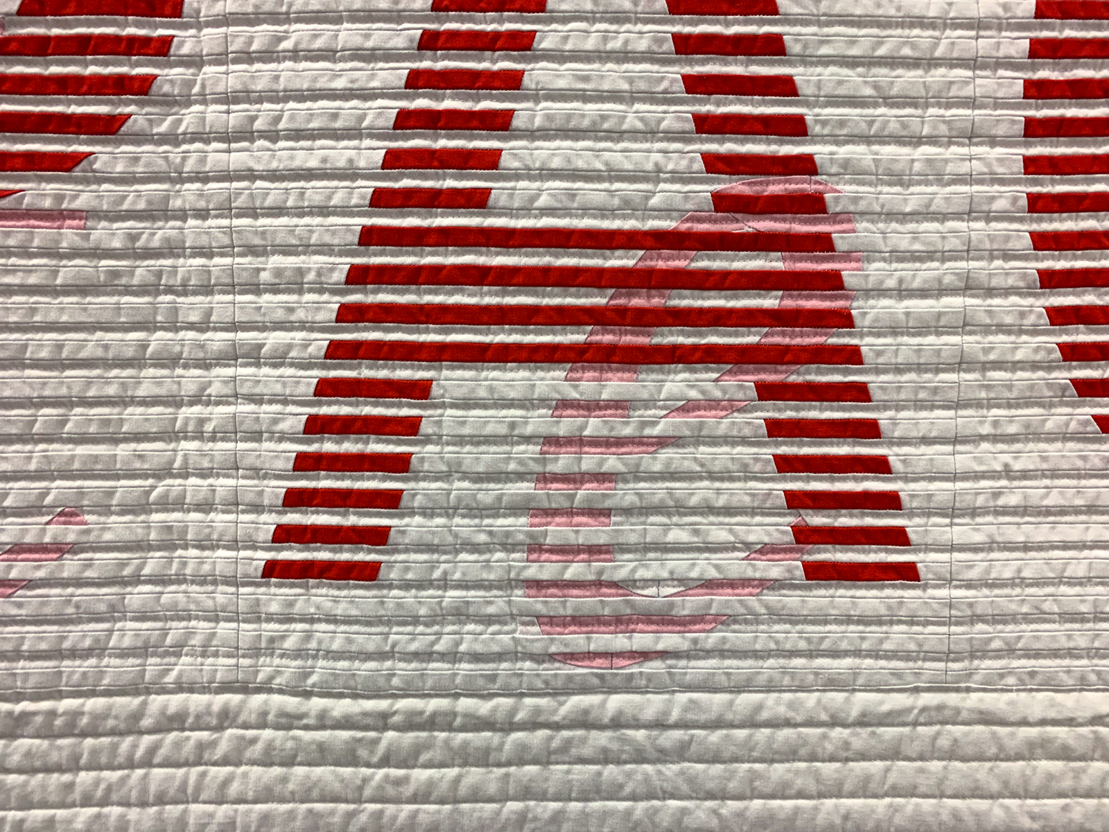 detail of Modern Quilt pieced with tiny strips intertwined to spell out Impact in large letters and Intent in small letters. 