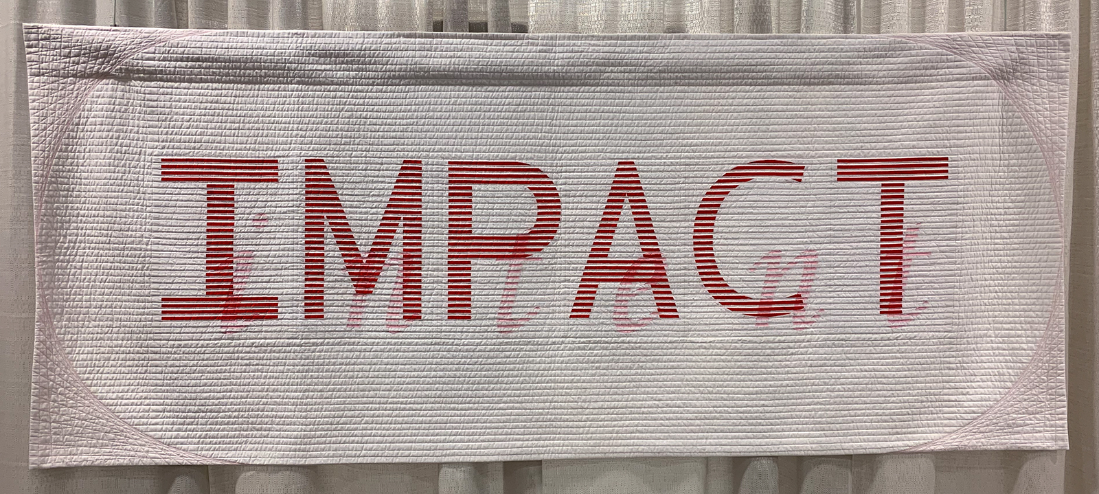 Modern Quilt pieced with tiny strips intertwined to spell out Impact in large letters and Intent in small letters. 