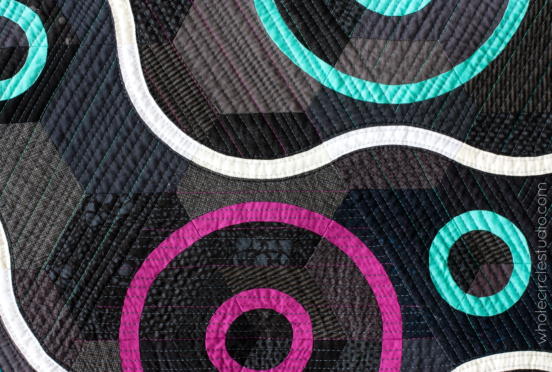detail of modern minimalist quilt with a dark background and a white curvy line moving around magenta, blue, and aqua circles