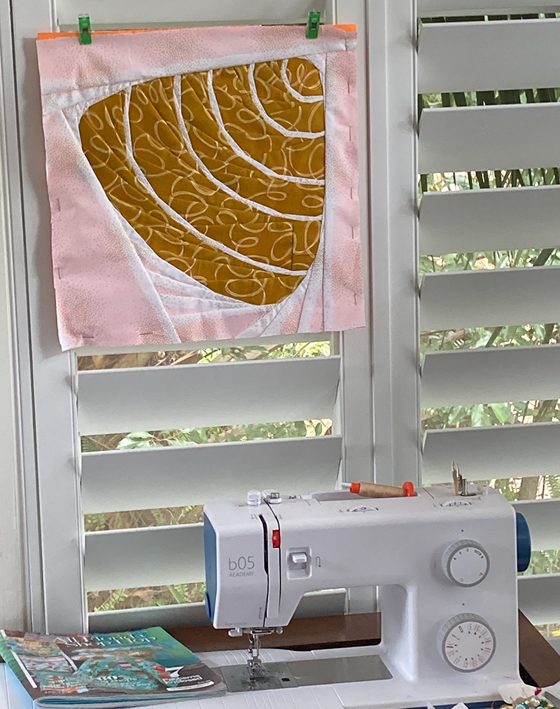 quilt block of an abstract Shell Shell hanging on a wall with a sewing machine in front.