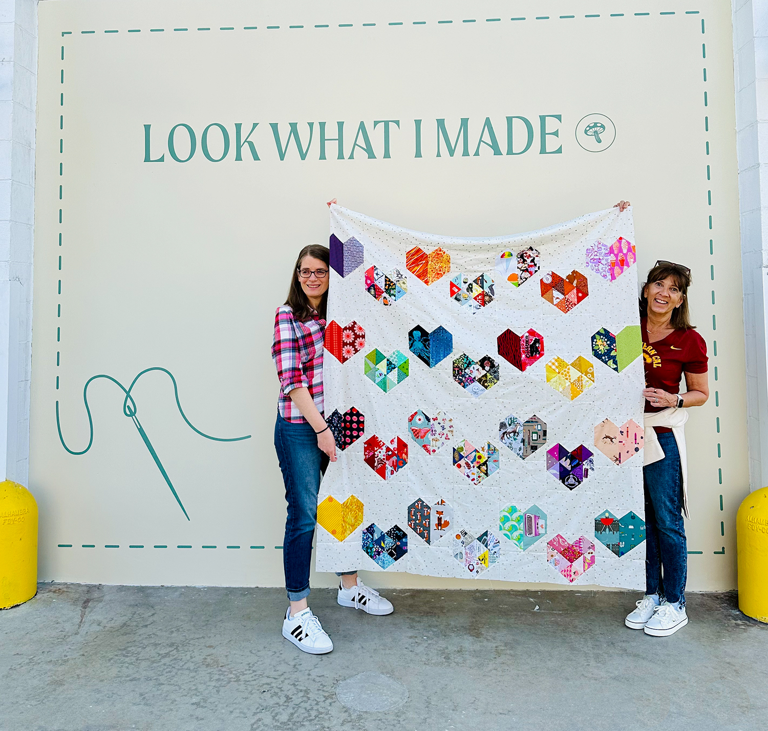 two women holding up a quilt top with hearts on it