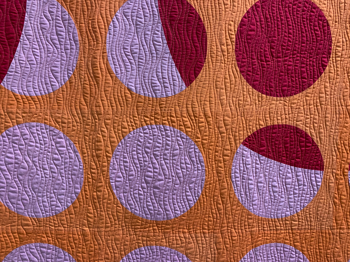 detail of modern quilt: red, pink, and orange quilt with lots of circles
