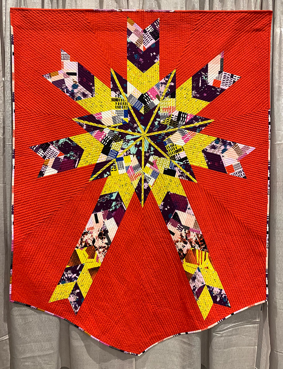 scrappy quilt of giant star, red background with black, white, and yellow