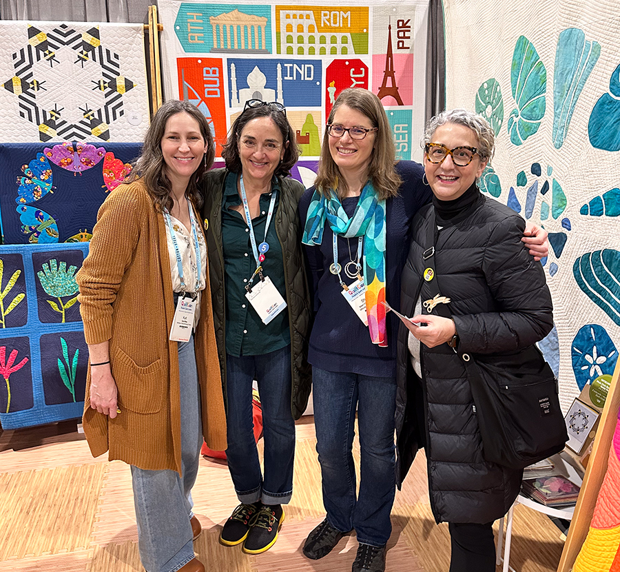 four women smiling in front of quilts