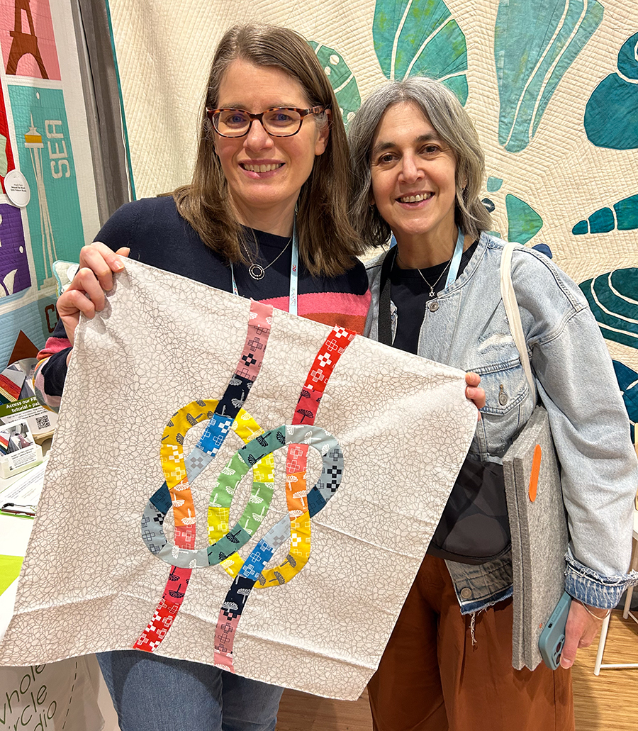 two women smiling holding a quilt top