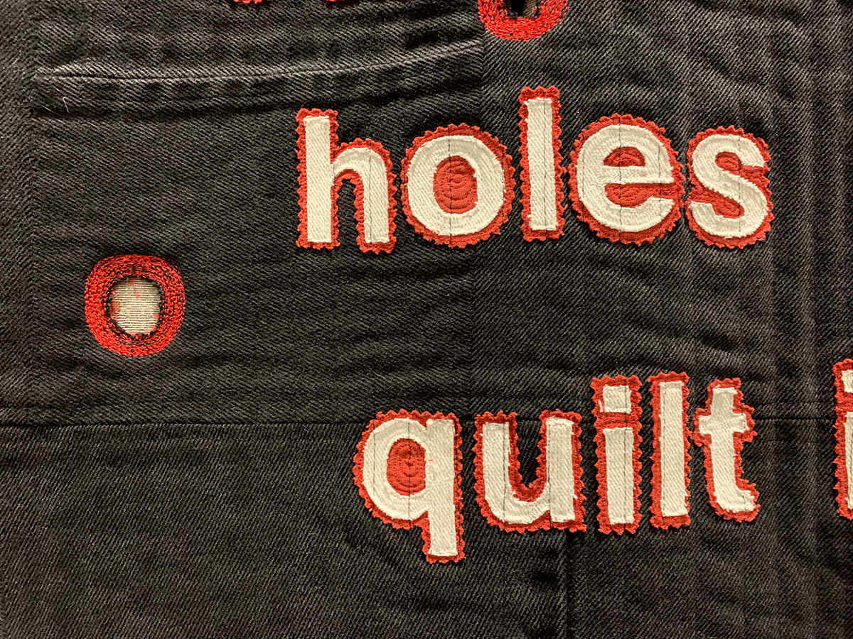 detail of quilt with the words "The number of holes in this quilt is the number that can be shot by an assault riffle in the time it takes to read this."