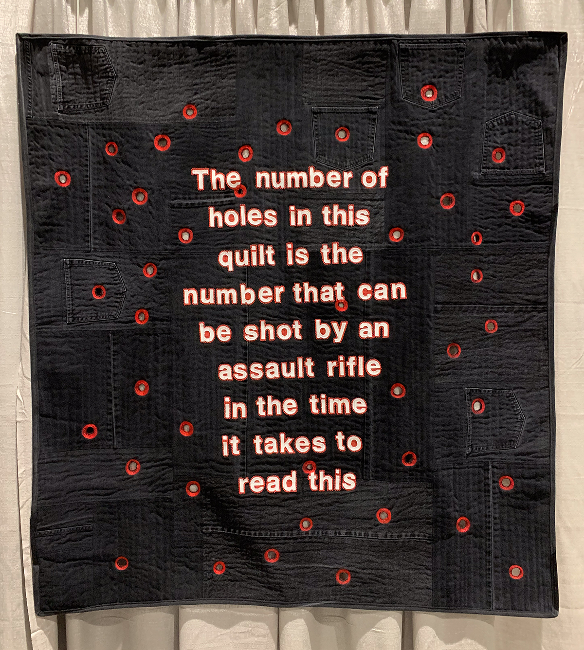 quilt with the words "The number of holes in this quilt is the number that can be shot by an assault riffle in the time it takes to read this."
