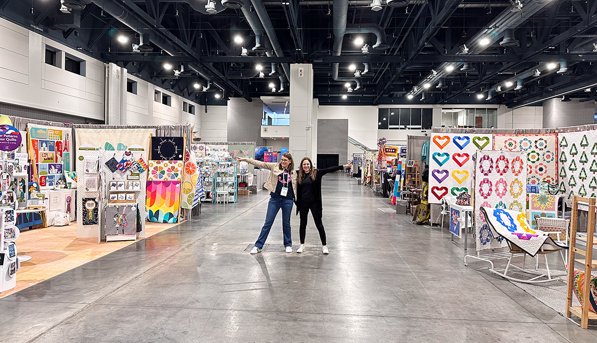 two woman in a convention center pointing in opposite directions