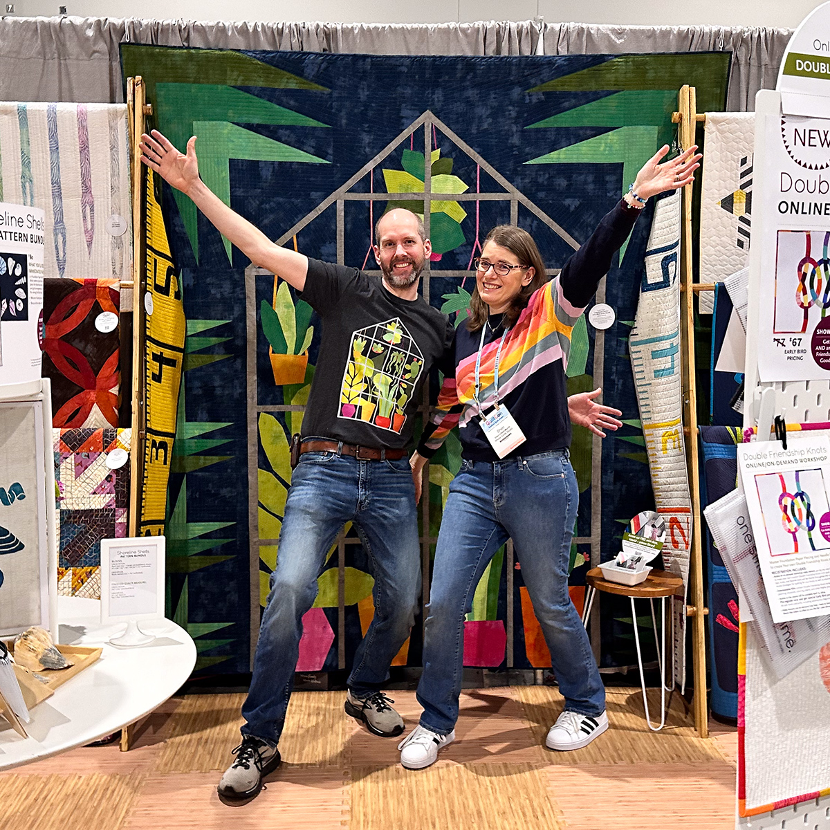 woman and man with hands up in front of greenhouse quilt