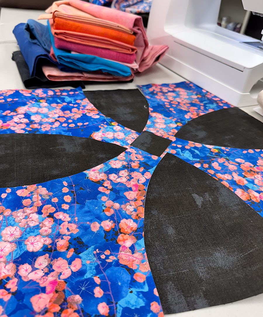 a quilt block with round petals in progres with a stack of fabric in the background