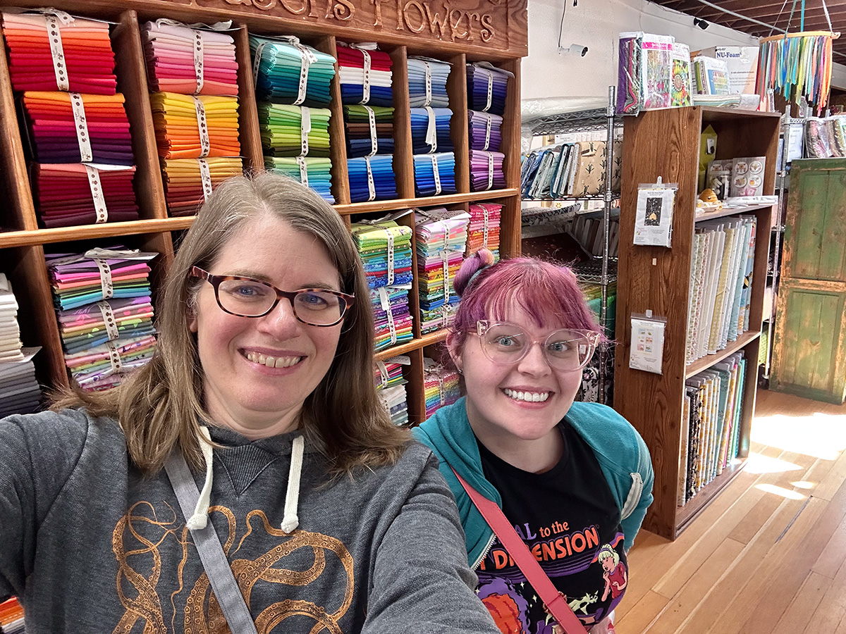 two women smiling in front of a display of fabric in a store