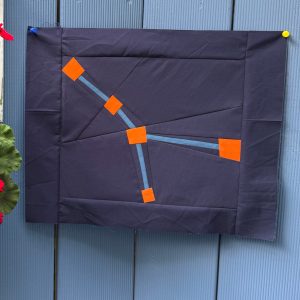 Cancer constellation zodiac quilt block hanging on a blue fence