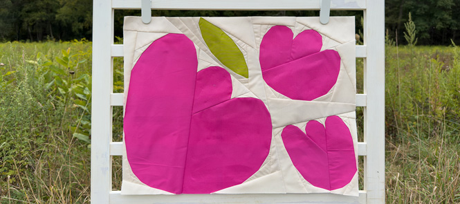 quilt block with pink flowers and green leaves on a ladder in a field