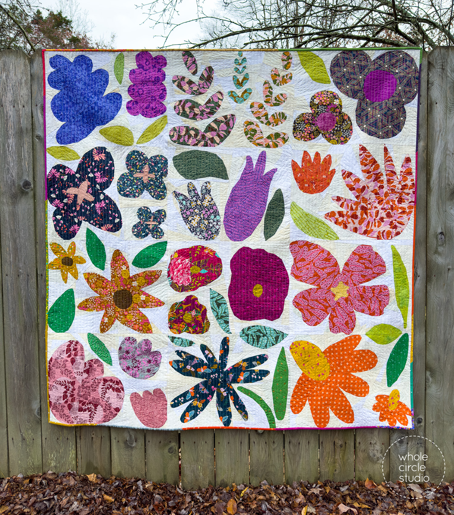 Scrappy Wildflower Remix quilt showing 12 colorful flower blocks, green leaves, scrappy binding, and a white/neutral scrappy patchwork background, foundation paper pieced.