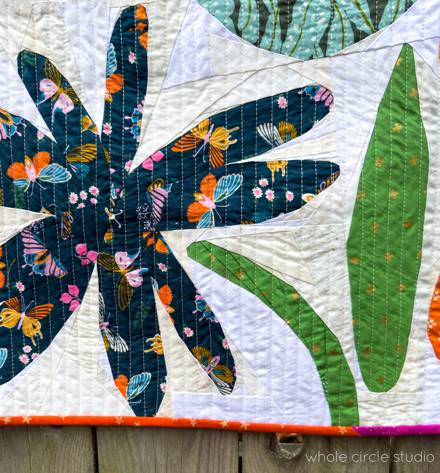 Scrappy Wildflower Remix quilt close-up showing a colorful flower block with scrappy binding and a white/neutral scrappy background, foundation paper pieced.