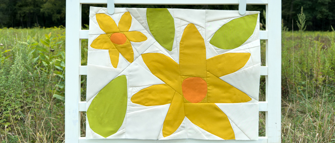 quilt block with yellow and orange flowers and green leaves on a ladder in a field