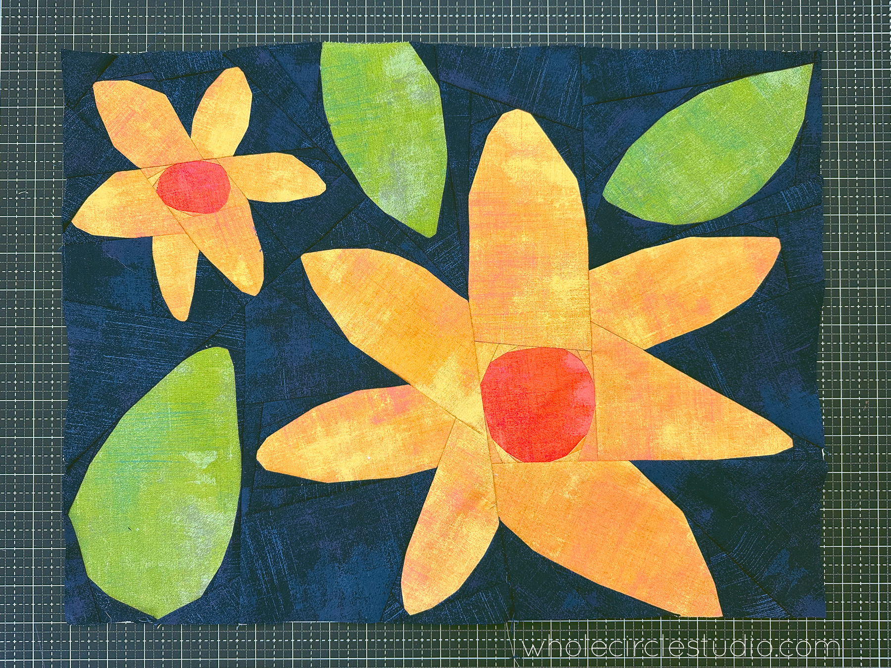 abstract yellow and orange flower quilt block on a navy background sitting on a cutting mat