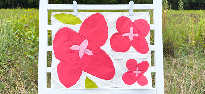 quilt block with pink flowers and green leaves on a ladder in a field