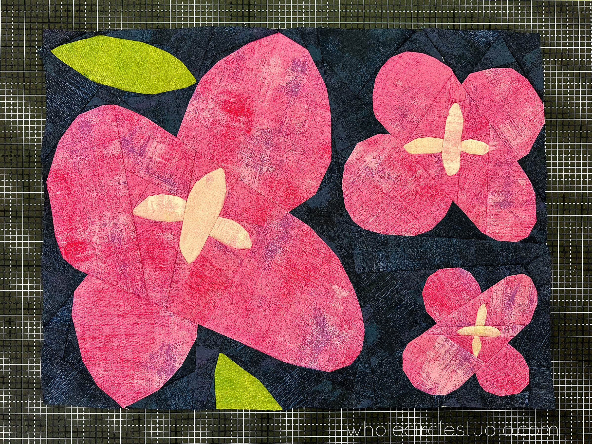 abstract pink flowers quilt block on a navy background sitting on a cutting mat