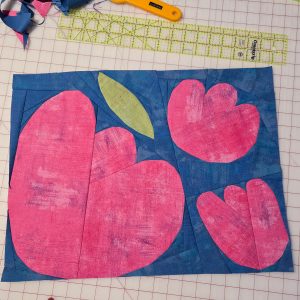 modern flower quilt block made with textured fabrics on a cutting mat with rulers and rotary cutter