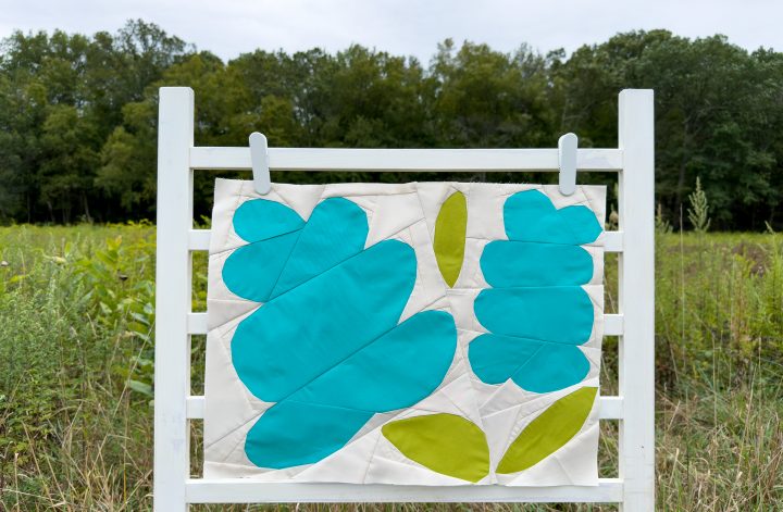 quilt block with blue flowers and green leaves on a ladder in a field