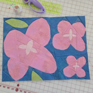 Wildflower quilt block with geometric shapes on a cutting mat with quilting tools