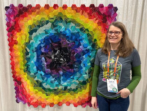 woman smiling and standing in front of colorful hexagon quilt