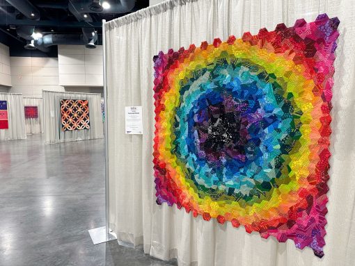 colorful hexagon quilt hanging in a quilt show