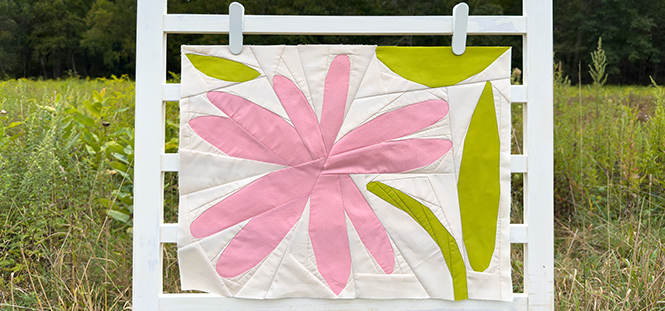 quilt block with pink flower and green leaves on a ladder in a field
