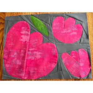 three foundation paper pieced flowers made using magenta fabric on a gray background