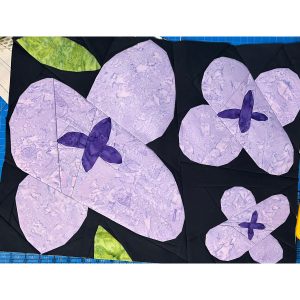 Wildflower quilt block with geometric shapes made with purple and green batik fabric