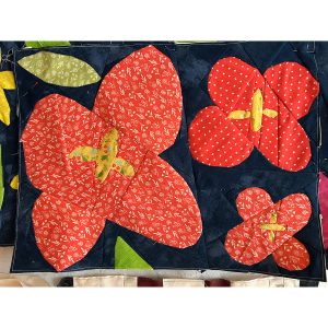 Wildflower quilt block with geometric shapes made orange and green floral fabric on a navy blue background