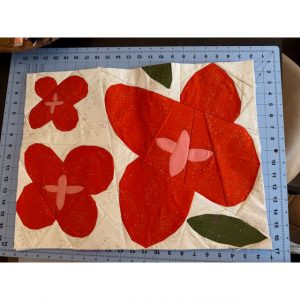 Wildflower quilt block with geometric shapes made with red, pink, and green fabric on a cutting mat