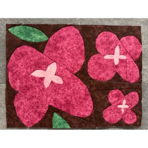 Wildflower quilt block with geometric shapes made with magenta, pink, green, and brown fabrics