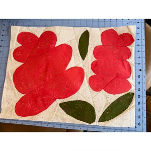 large foundation paper pieced flower quilt block made with red, green and white fabric on a cutting mat